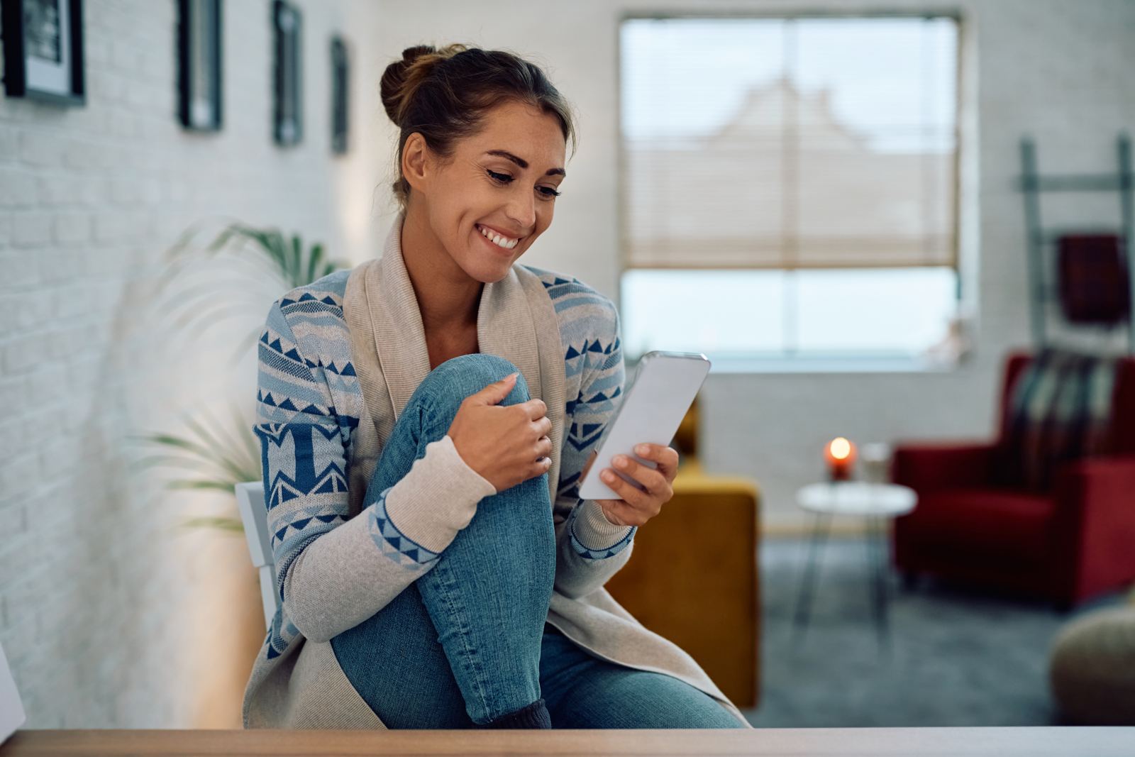 Happy woman texting on cell phone while relaxing at home