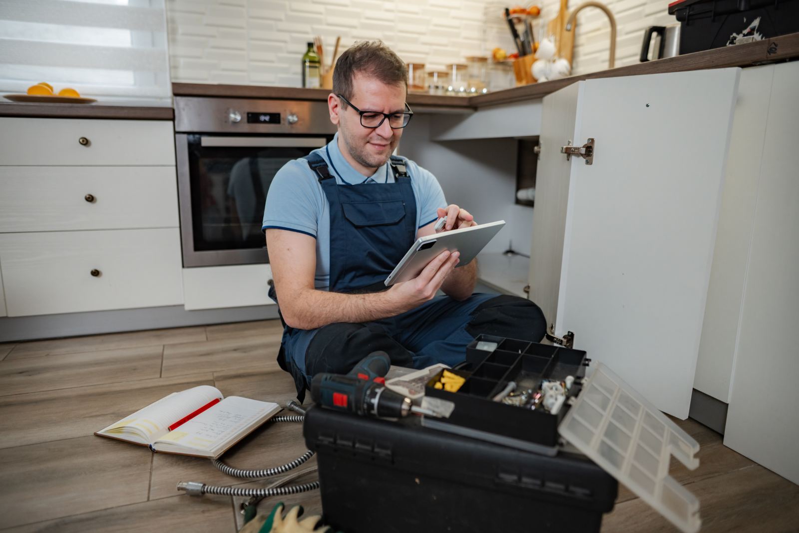 Plumber using digital tablet repairing pipe under kitchen sink
